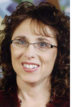 Headshot of a smiling woman with long, curly dark hair, blue eyes, and glasses.