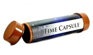 Cylindrical time capsule with brown end caps, one of which is open. Its dark blue body has a starry pattern and a white label in the center that reads "TIME CAPSULE".